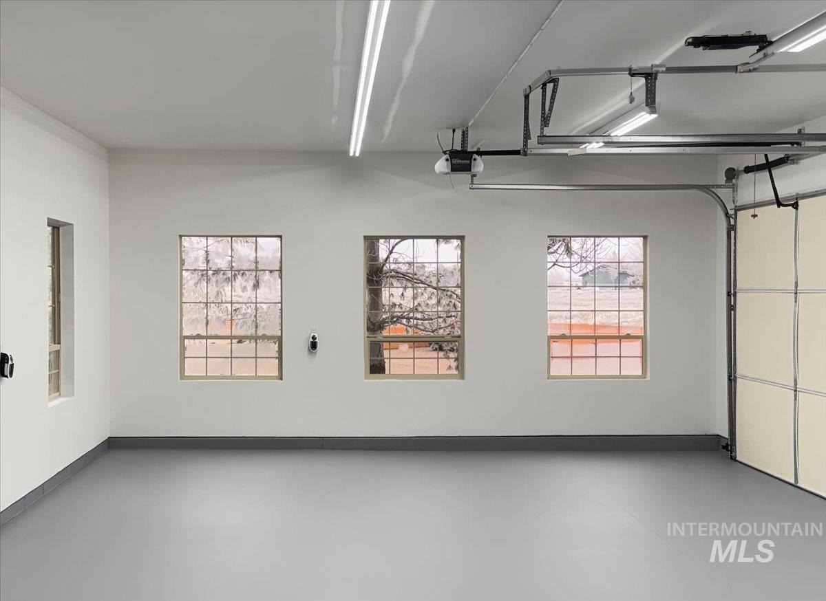 Spacious garage featuring a light gray epoxy floor coating, white painted walls, and multiple grid-pattern windows