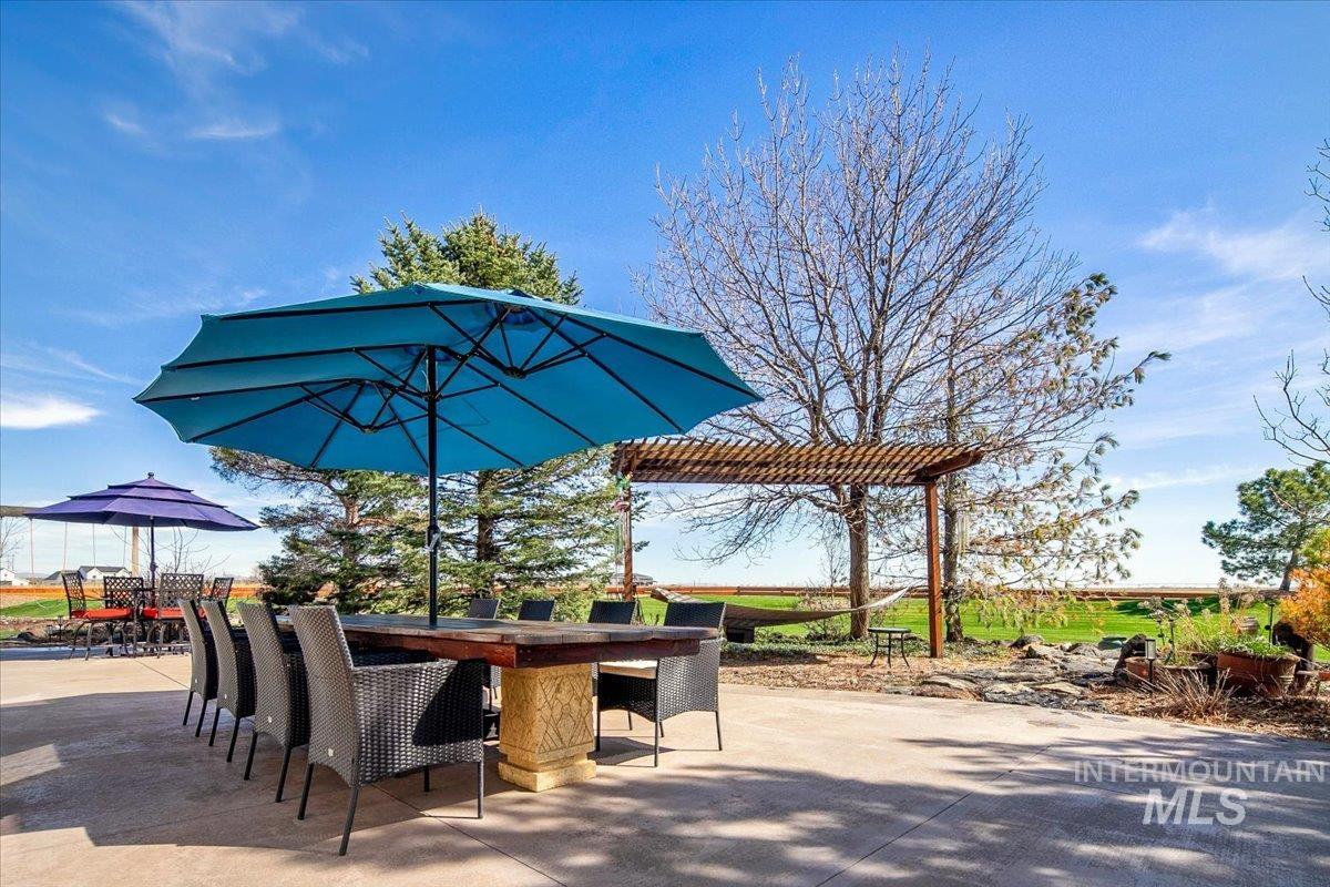 Expansive patio featuring a large outdoor dining table, multiple seating areas, a wooden pergola, and mature trees