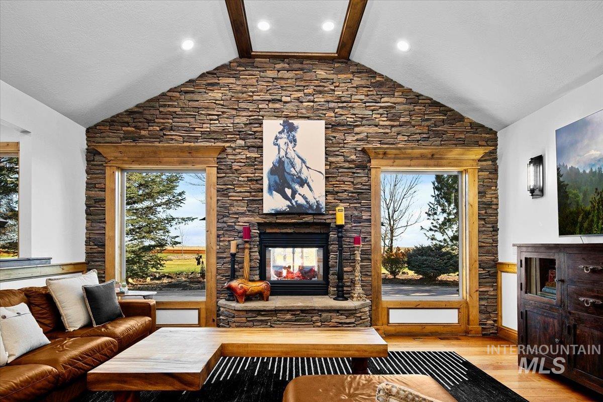 Vaulted ceiling with exposed wood beams, a stone-clad fireplace, and natural wood window trim