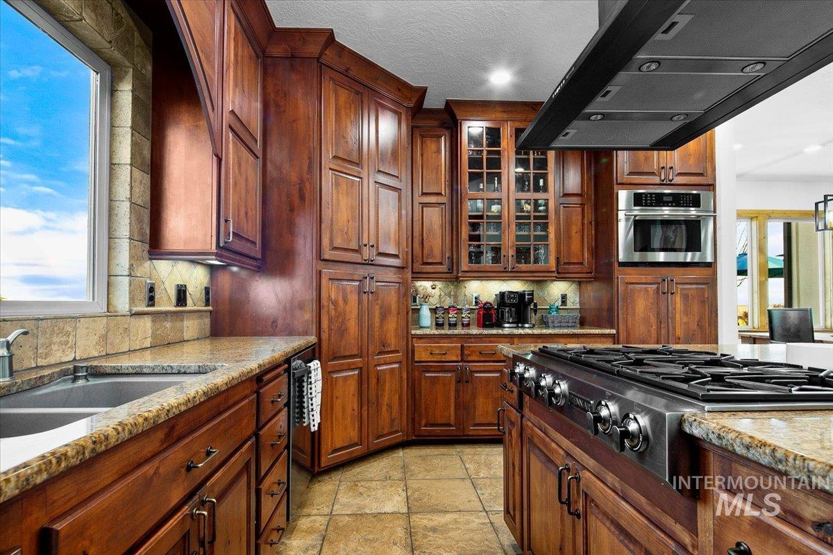 Expansive kitchen featuring rich wood cabinetry, granite countertops, stainless steel appliances, a large gas range with hood, and ceramic tile flooring