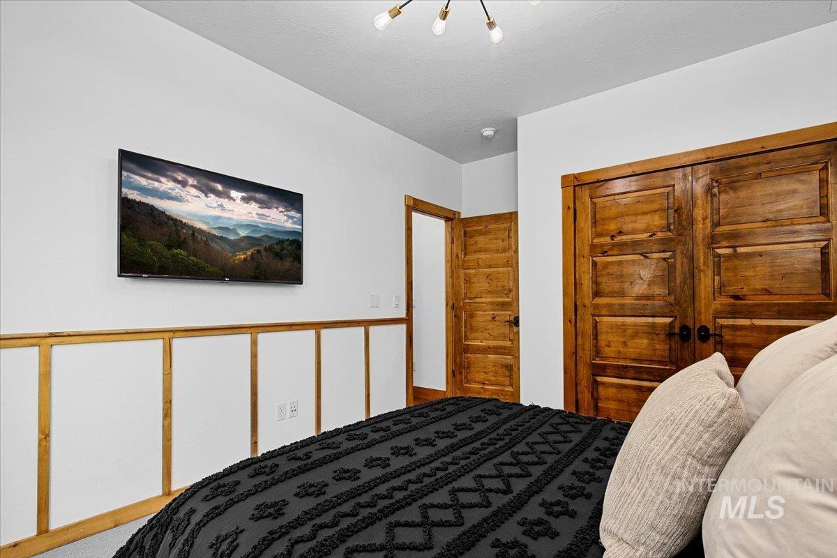 Bedroom featuring a mounted television and white wainscoting with wood trim