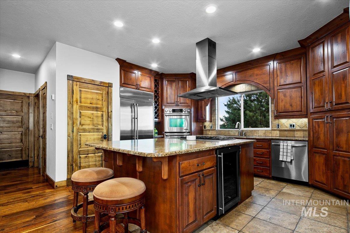 Kitchen featuring wood cabinetry, granite countertops, stainless steel appliances, a center island with built-in beverage cooler, and recessed lighting
