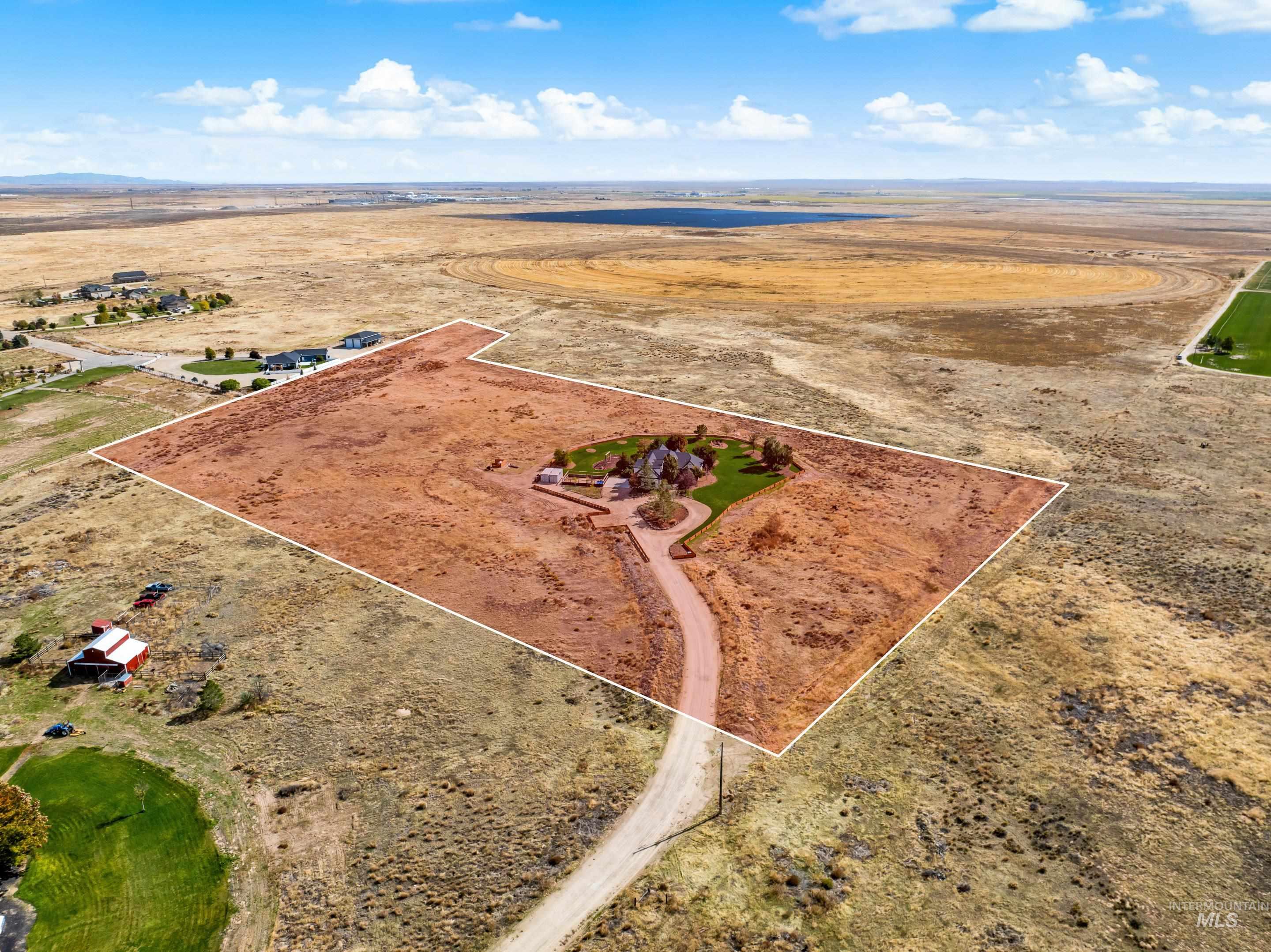 Expansive parcel featuring a large custom residence, circular driveway, substantial green lawn areas, and surrounded by open, undeveloped land