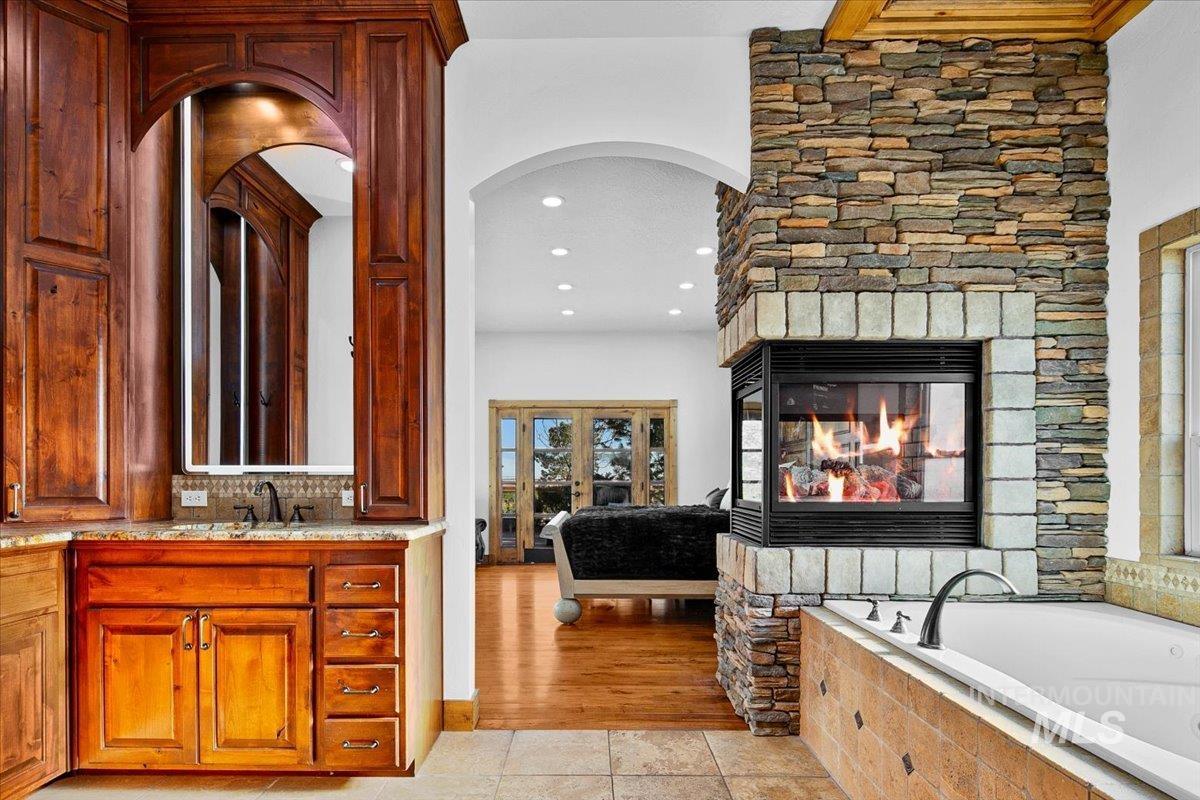 Expansive stone-clad fireplace with a three-sided glass enclosure, integrated into a soaking tub surround