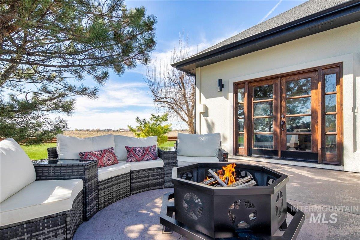 Outdoor patio featuring a hexagonal fire pit, direct access through double French doors, and a partial view of a green landscape