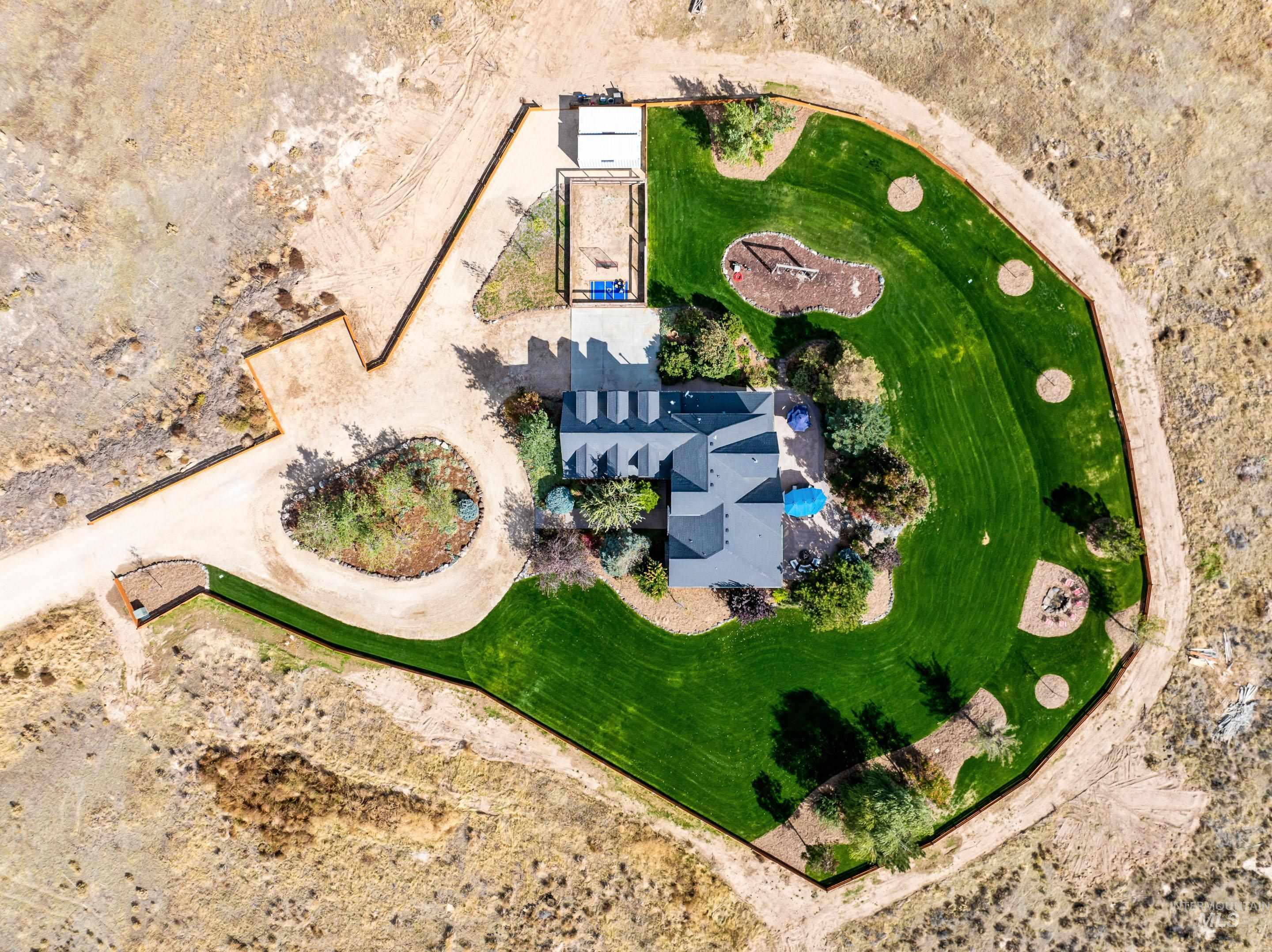 Expansive landscaped property featuring a large green lawn, a circular driveway, multiple outbuildings, and a dedicated fire pit area