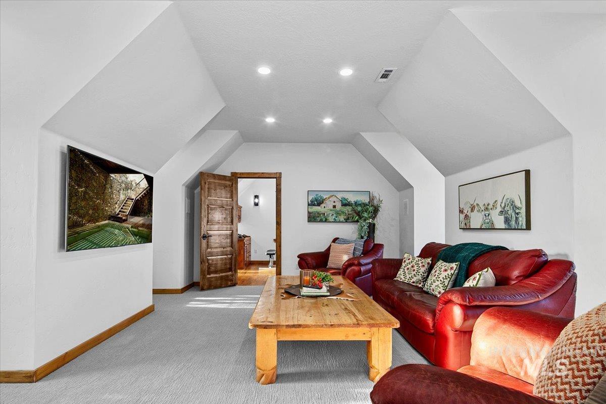 Spacious room featuring vaulted ceilings, recessed lighting, light gray carpeting, and warm wood trim
