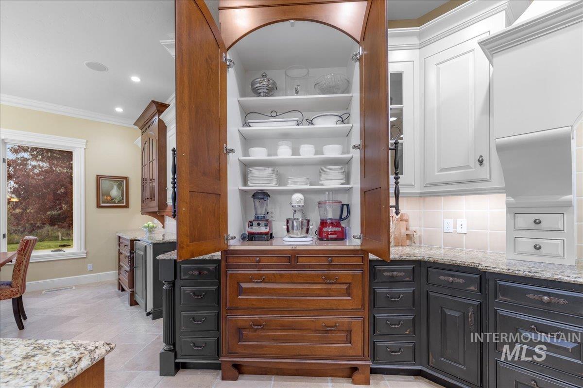 Bar area with light stone counters, white cabinetry, crown molding, open shelves, and backsplash