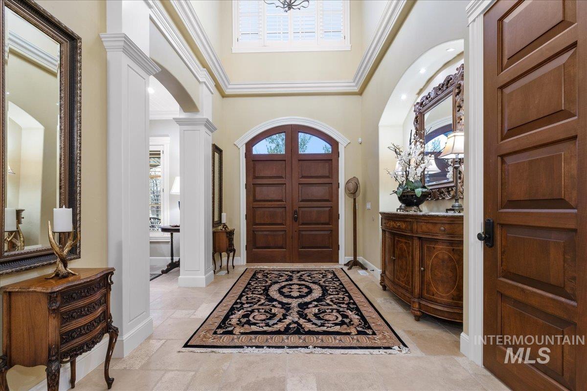 Entryway with arched walkways, a towering ceiling, decorative columns, ornamental molding, and stone tile flooring