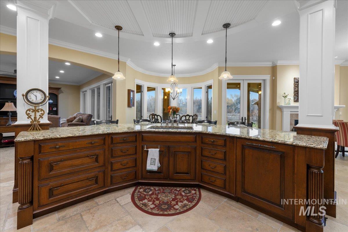Kitchen featuring open floor plan, ornate columns, hanging light fixtures, recessed lighting, and light stone counters