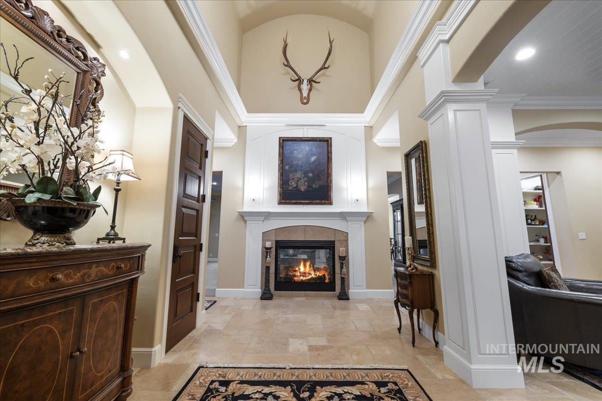 Entrance foyer with arched walkways, vaulted ceiling, crown molding, a fireplace, and stone tile flooring