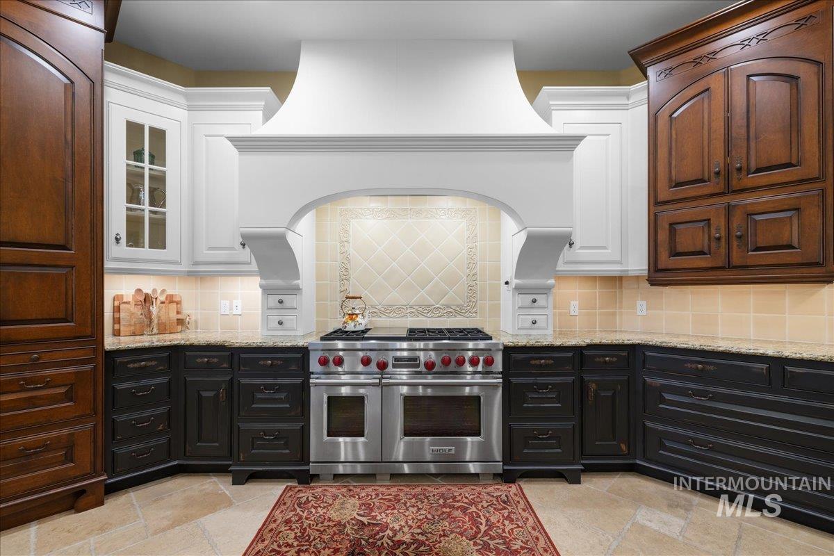 Kitchen featuring range with two ovens, stone tile flooring, light stone counters, and dark cabinets