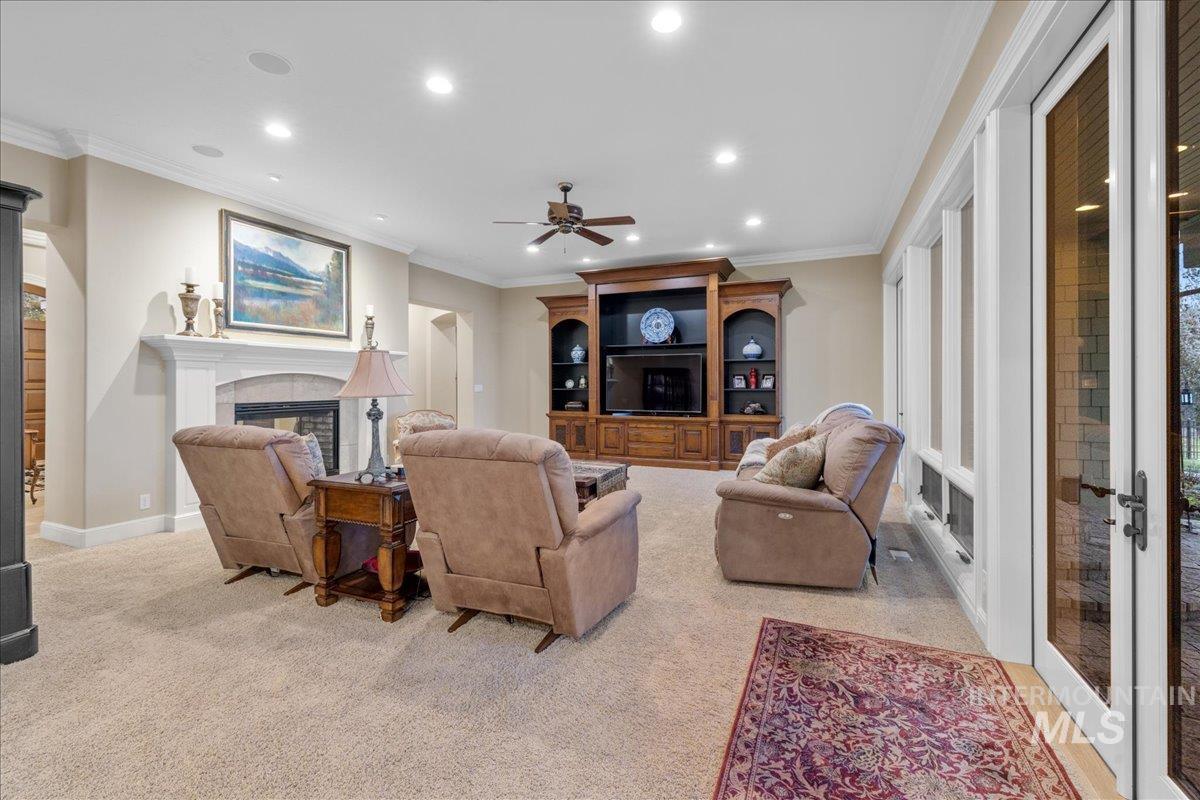 Living area with ornamental molding, a fireplace, recessed lighting, a ceiling fan, and light carpet