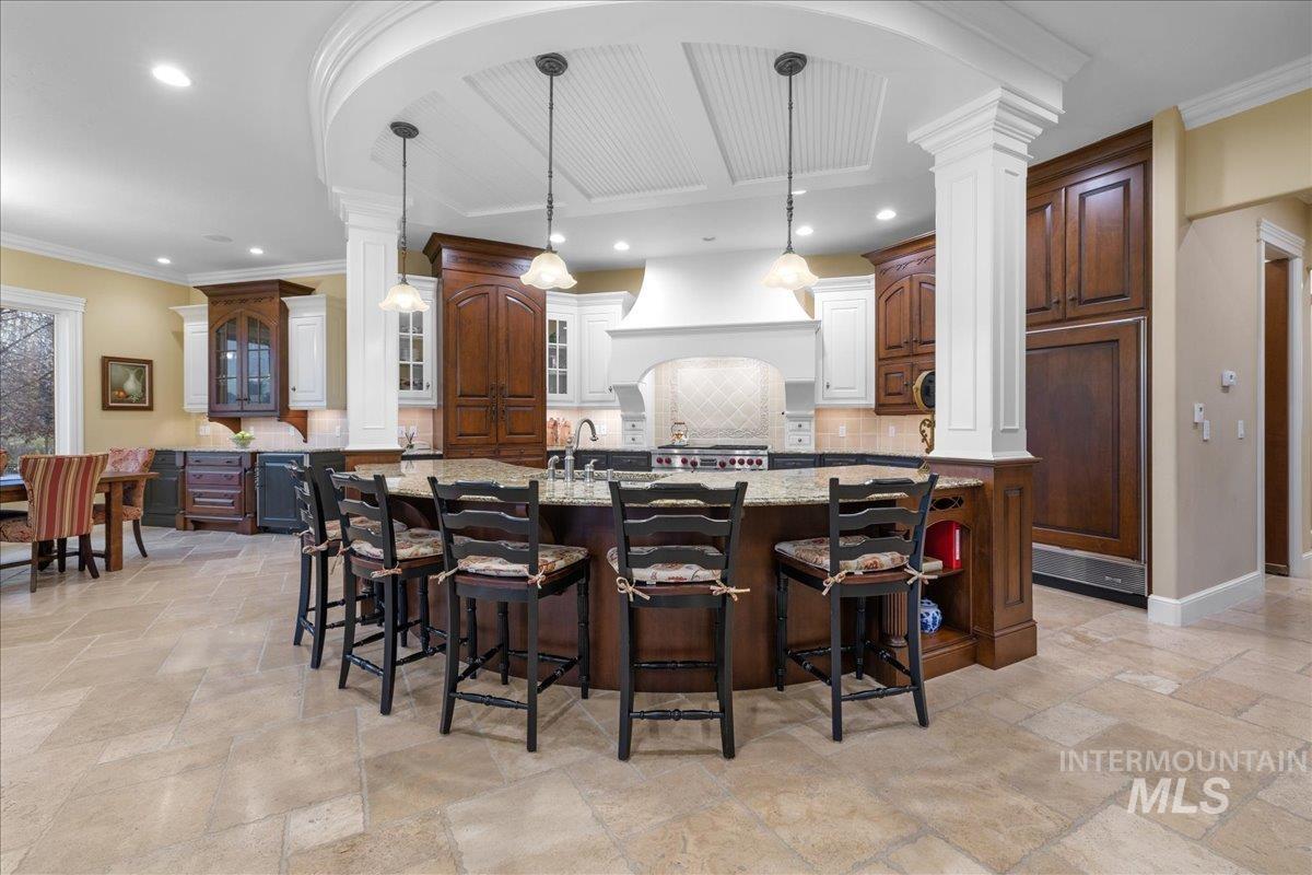 Kitchen featuring backsplash, a kitchen breakfast bar, decorative light fixtures, light stone counters, and ornamental molding