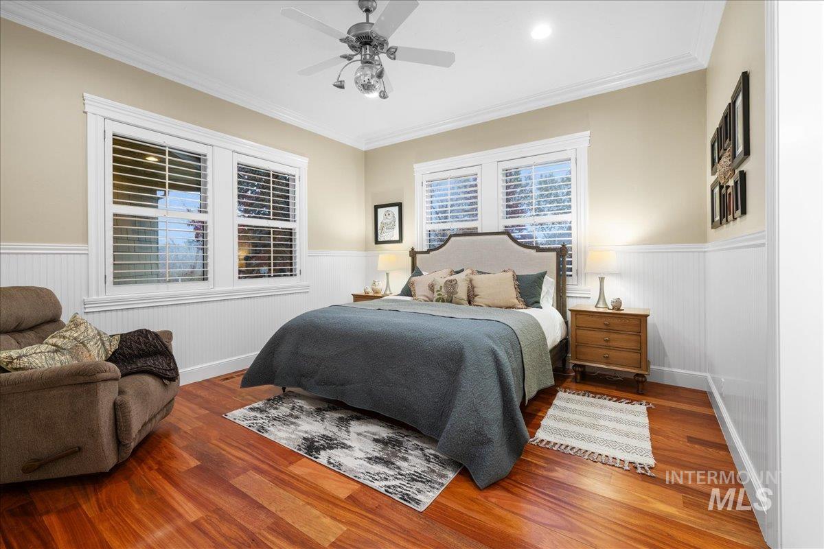 Bedroom featuring wood finished floors, wainscoting, a ceiling fan, and ornamental molding