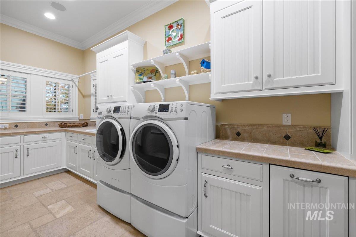 Washroom featuring crown molding, cabinet space, washer and clothes dryer, and stone tile floors