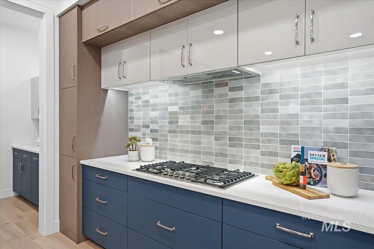 Kitchen with tasteful backsplash, blue cabinets, light wood-style floors, stainless steel gas cooktop, and white cabinets