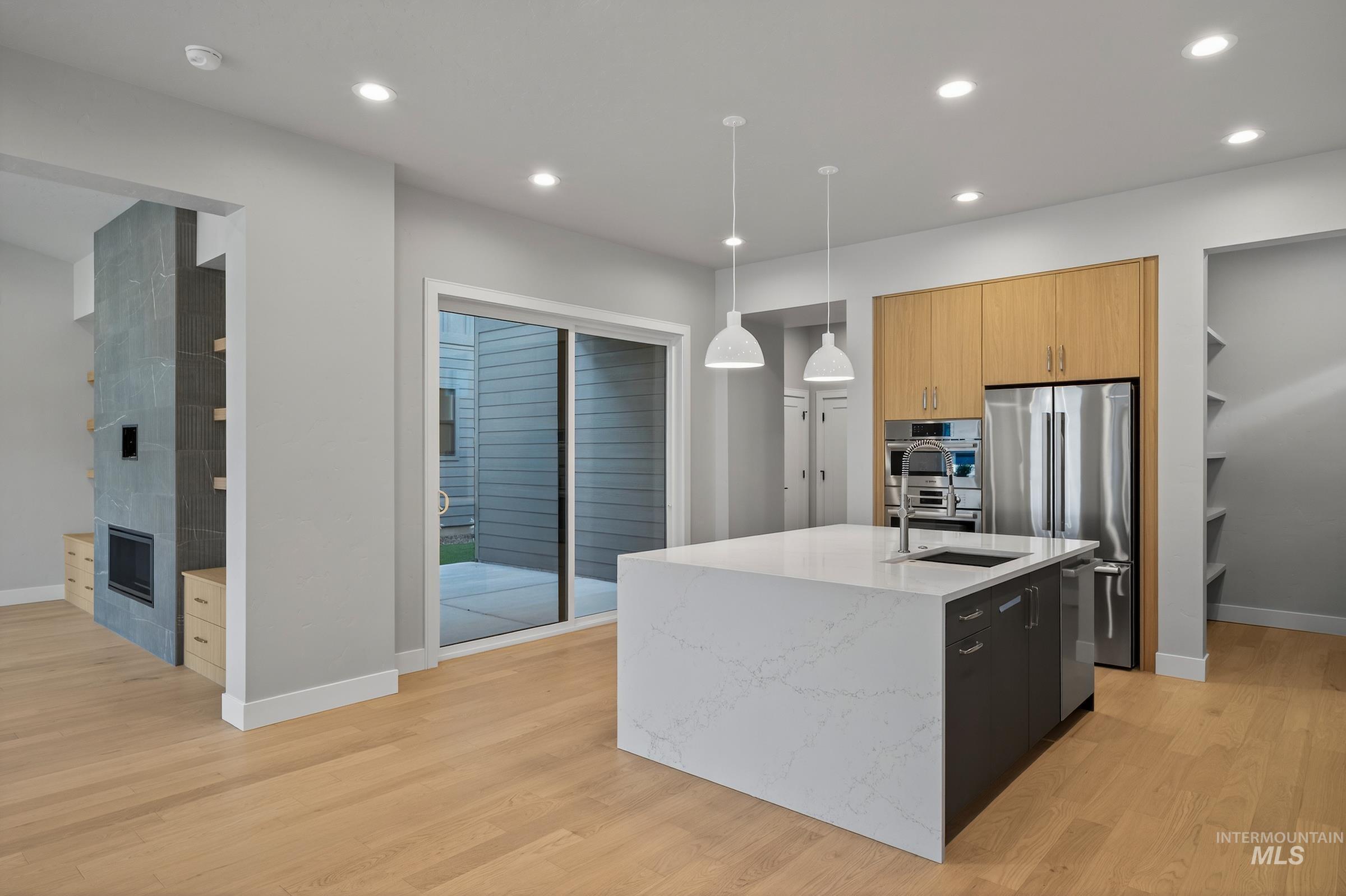 Kitchen featuring light stone countertops, recessed lighting, pendant lighting, appliances with stainless steel finishes, and a center island with sink