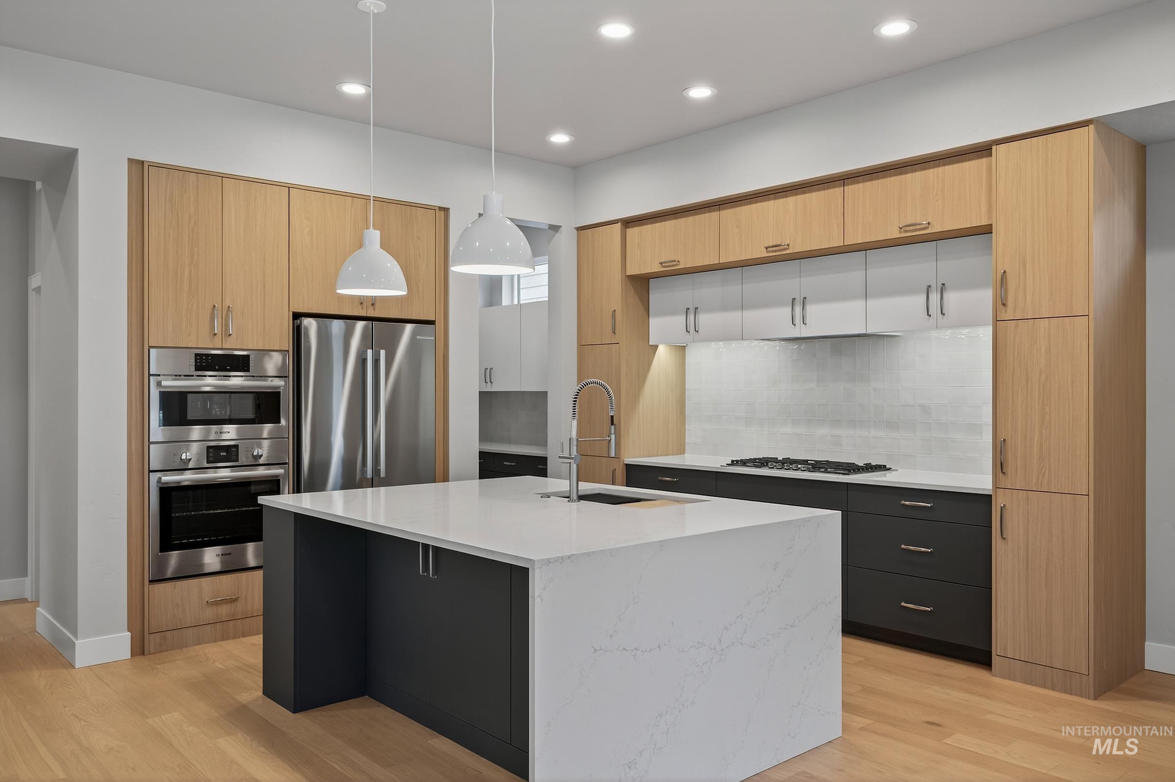 Kitchen featuring light brown cabinets, decorative light fixtures, light wood-style floors, appliances with stainless steel finishes, and recessed lighting