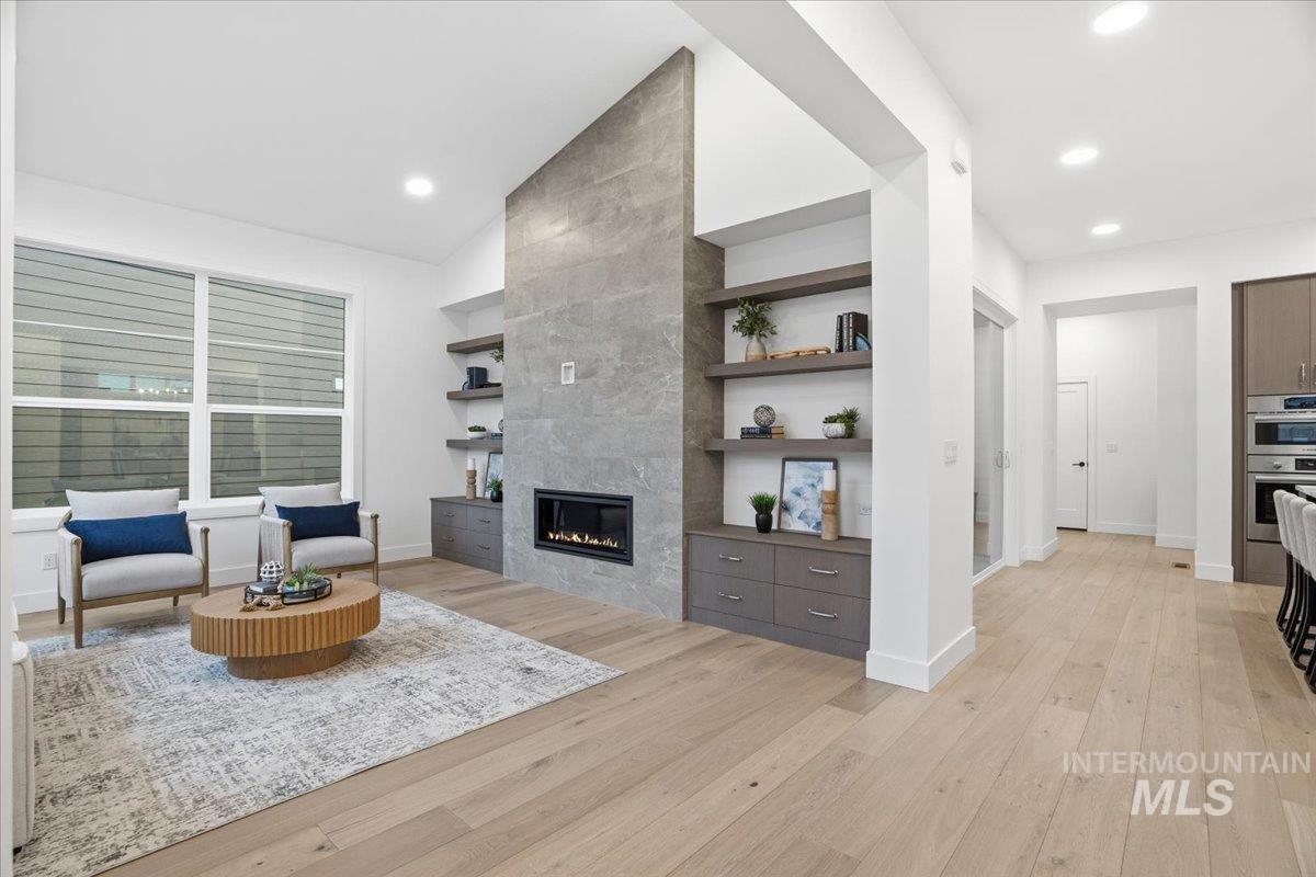 Living room with built in shelves, a tiled fireplace, light wood-type flooring, vaulted ceiling, and recessed lighting