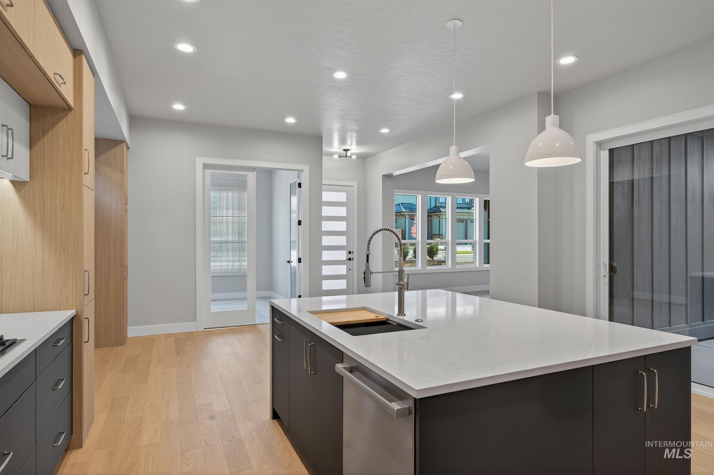 Kitchen with decorative light fixtures, light wood-style floors, recessed lighting, dark cabinetry, and light stone counters