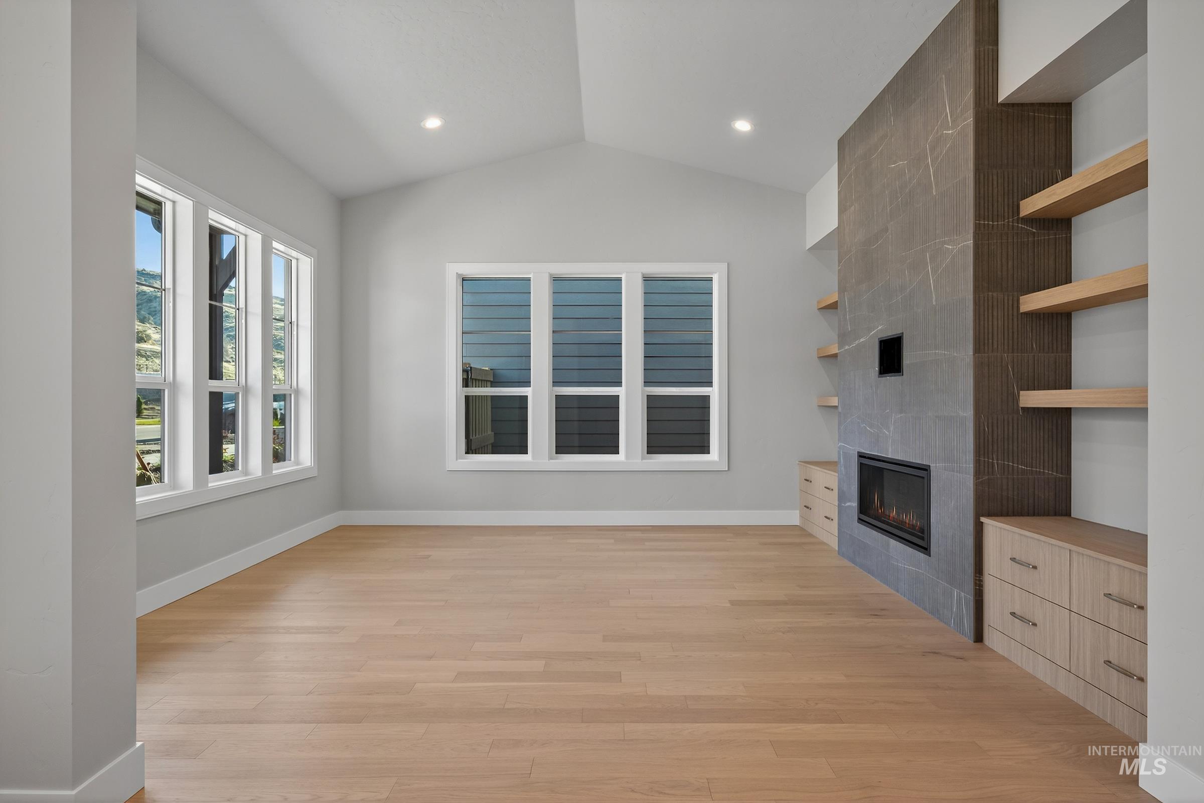 Unfurnished living room with a tiled fireplace, light wood-style flooring, lofted ceiling, and recessed lighting