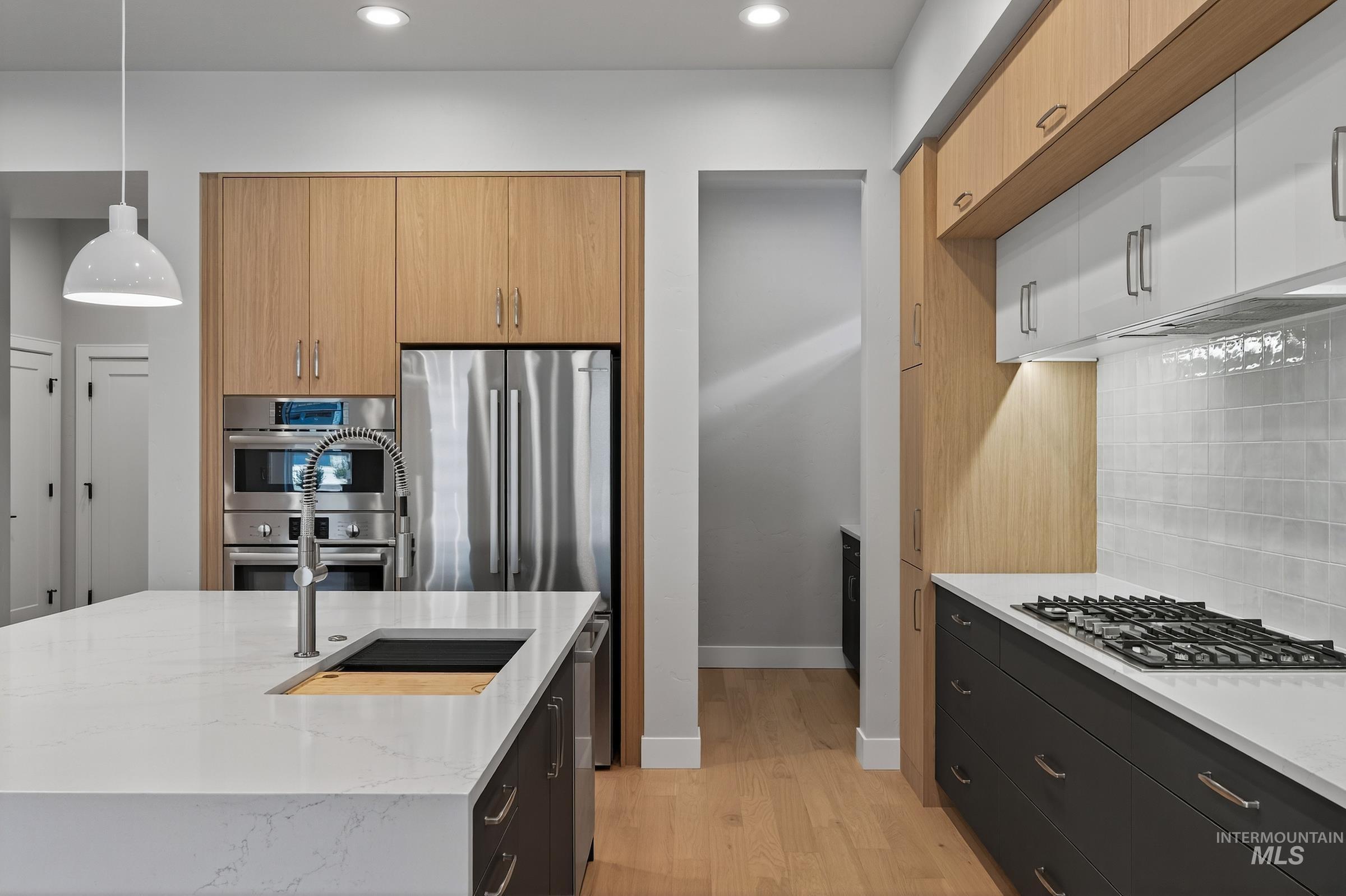 Kitchen with light stone counters, decorative light fixtures, light wood-type flooring, stainless steel appliances, and recessed lighting