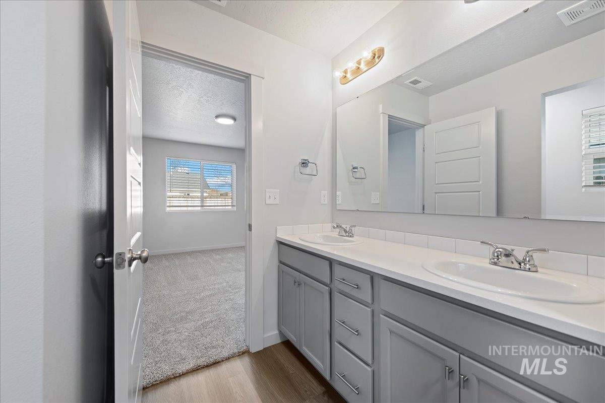 Full bath featuring double vanity, light wood-type flooring, and a textured ceiling