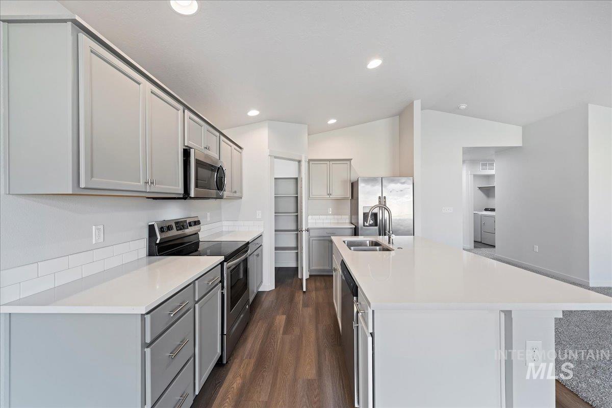 Kitchen featuring appliances with stainless steel finishes, an island with sink, dark wood-type flooring, lofted ceiling, and gray cabinets