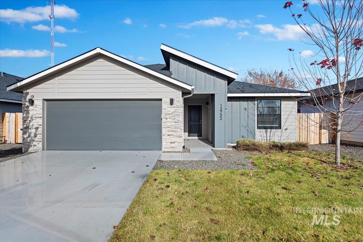 View of front of home with board and batten siding, driveway, a garage, and stone siding