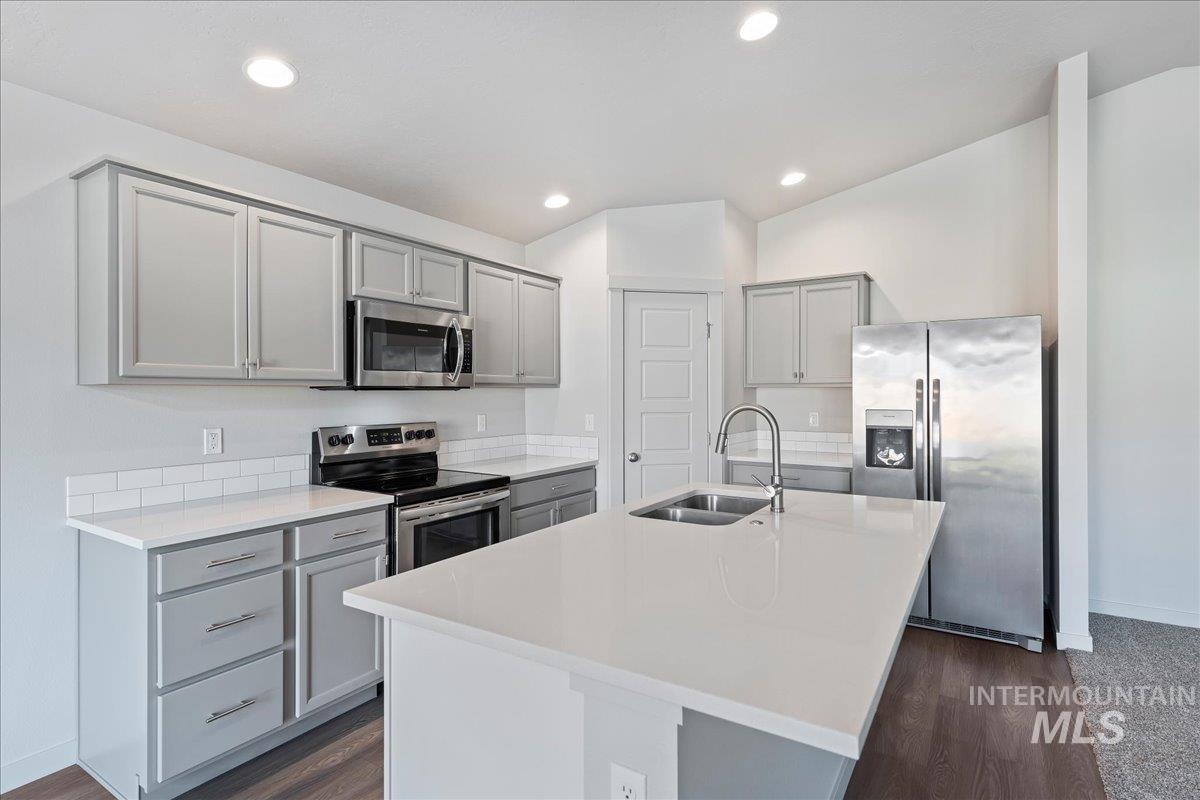 Kitchen with gray cabinetry, stainless steel appliances, a kitchen island with sink, recessed lighting, and dark wood-style flooring