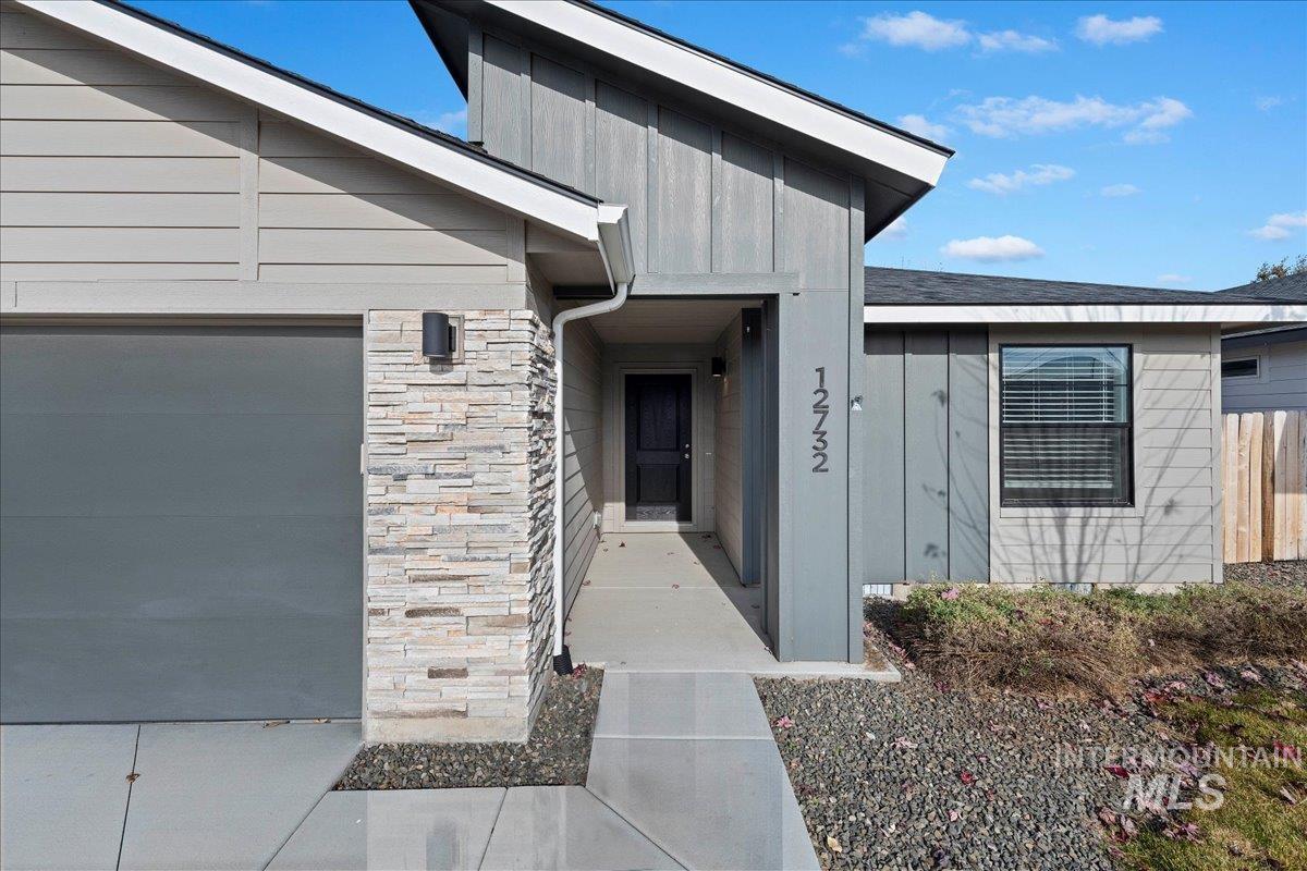 Entrance to property featuring stone siding, board and batten siding, a garage, and a shingled roof