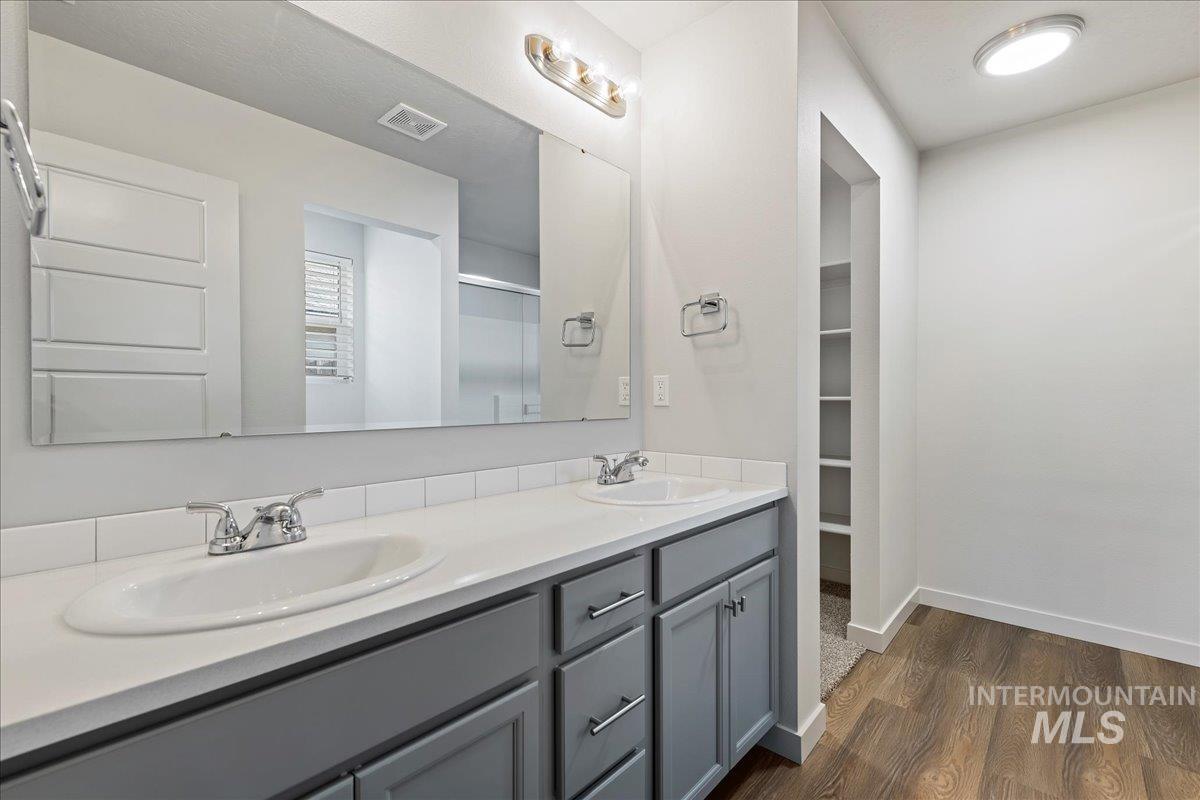 Bathroom with double vanity, a shower stall, dark wood-style flooring, and a spacious closet