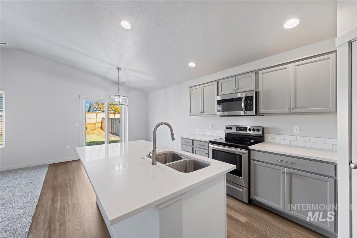Kitchen with gray cabinets, stainless steel appliances, lofted ceiling, a kitchen island with sink, and decorative light fixtures
