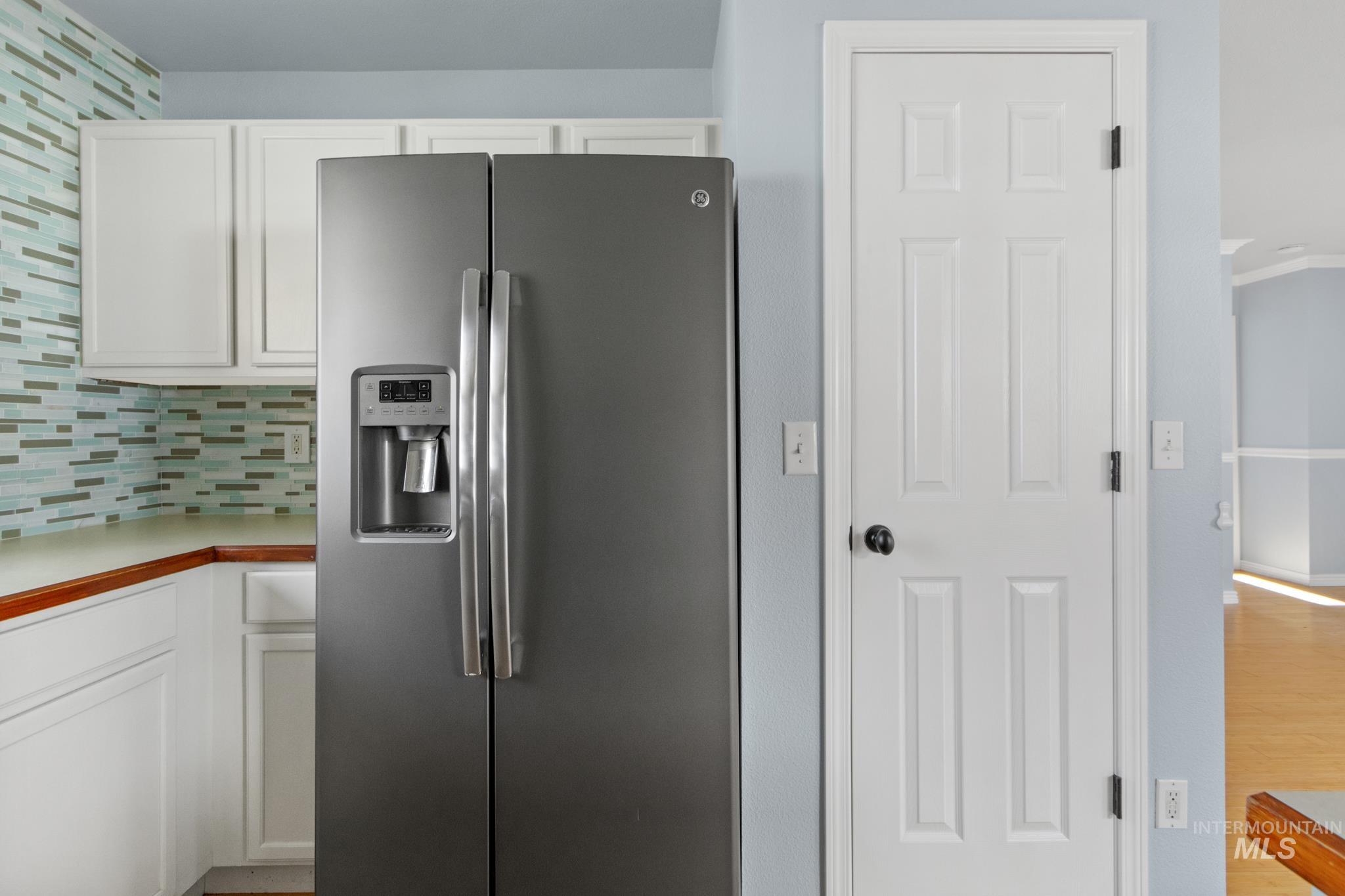 Kitchen featuring stainless steel refrigerator with ice dispenser, white cabinets, decorative backsplash, and light countertops