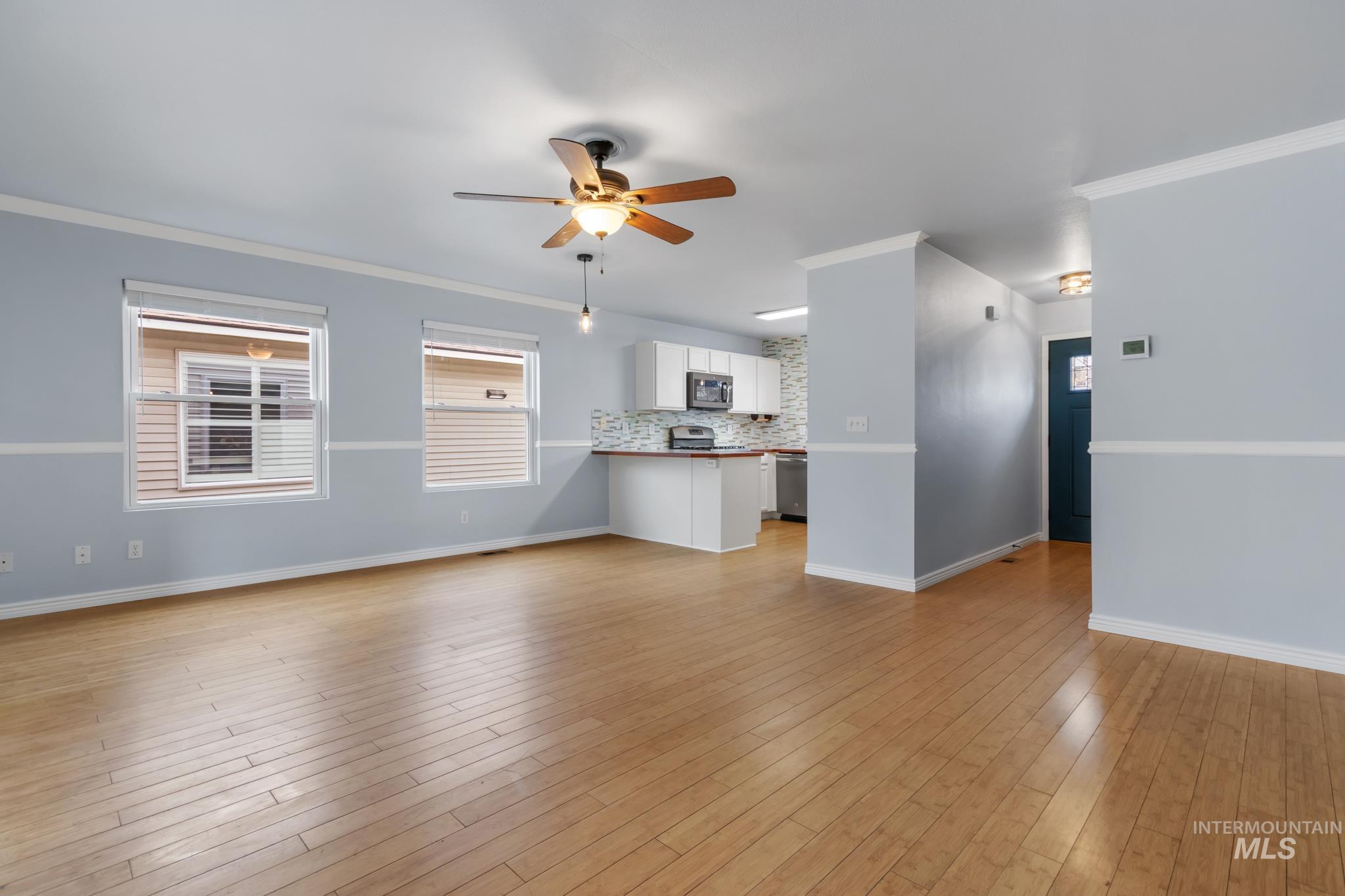 Unfurnished living room featuring crown molding, ceiling fan, and light wood-style flooring