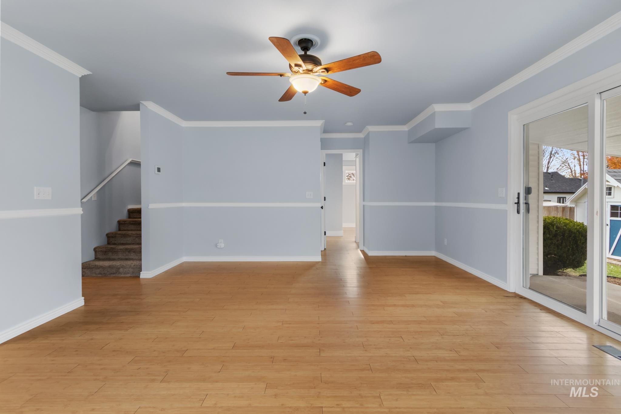 Unfurnished living room with crown molding, light wood finished floors, stairway, and ceiling fan