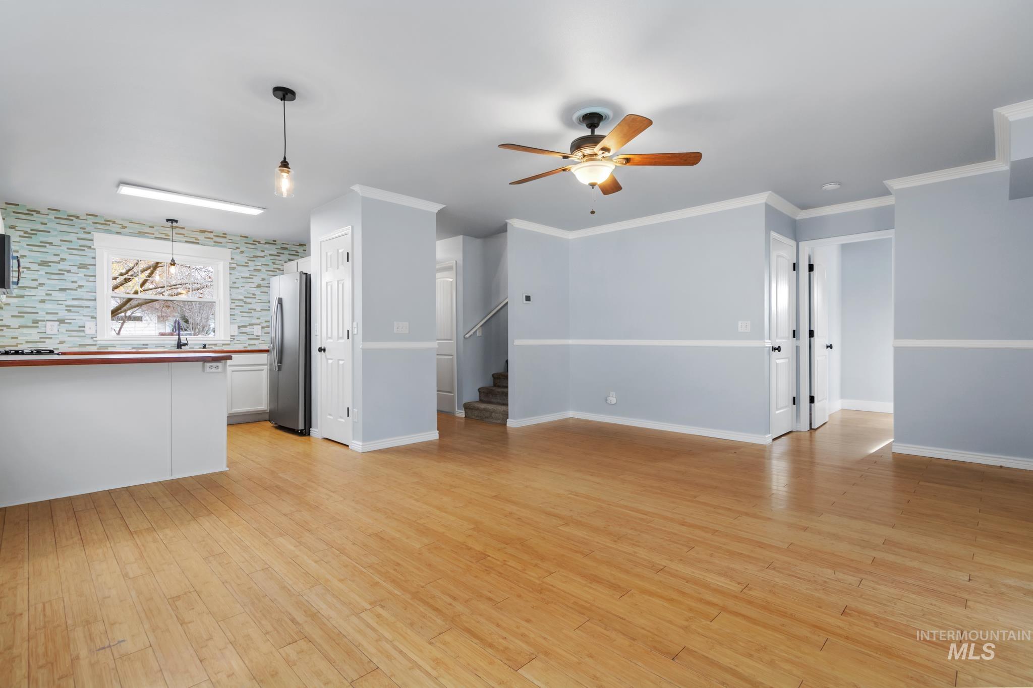 Unfurnished living room featuring light wood-style flooring, ceiling fan, stairway, and ornamental molding