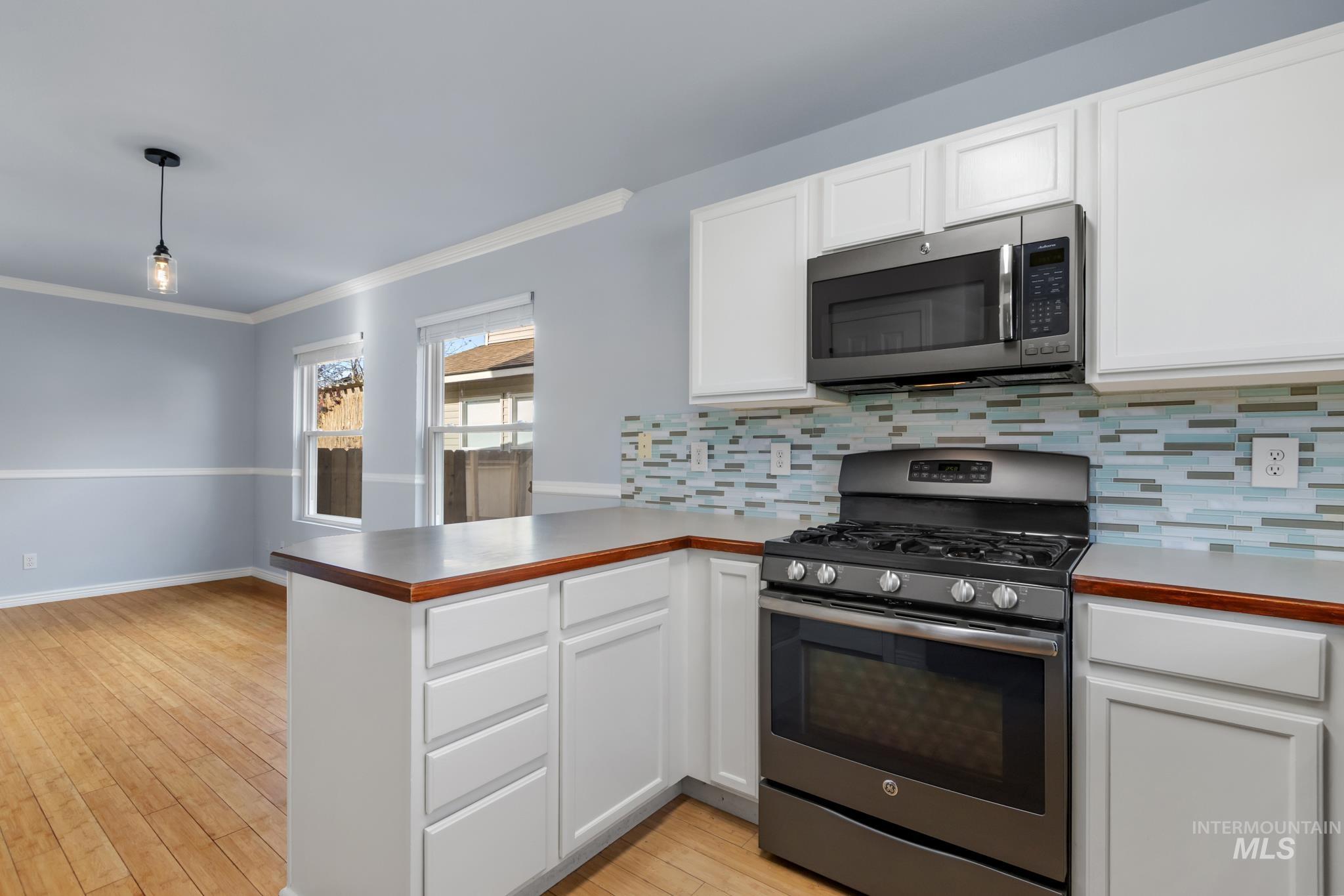 Kitchen featuring stainless steel appliances, white cabinets, a peninsula, crown molding, and light wood-type flooring
