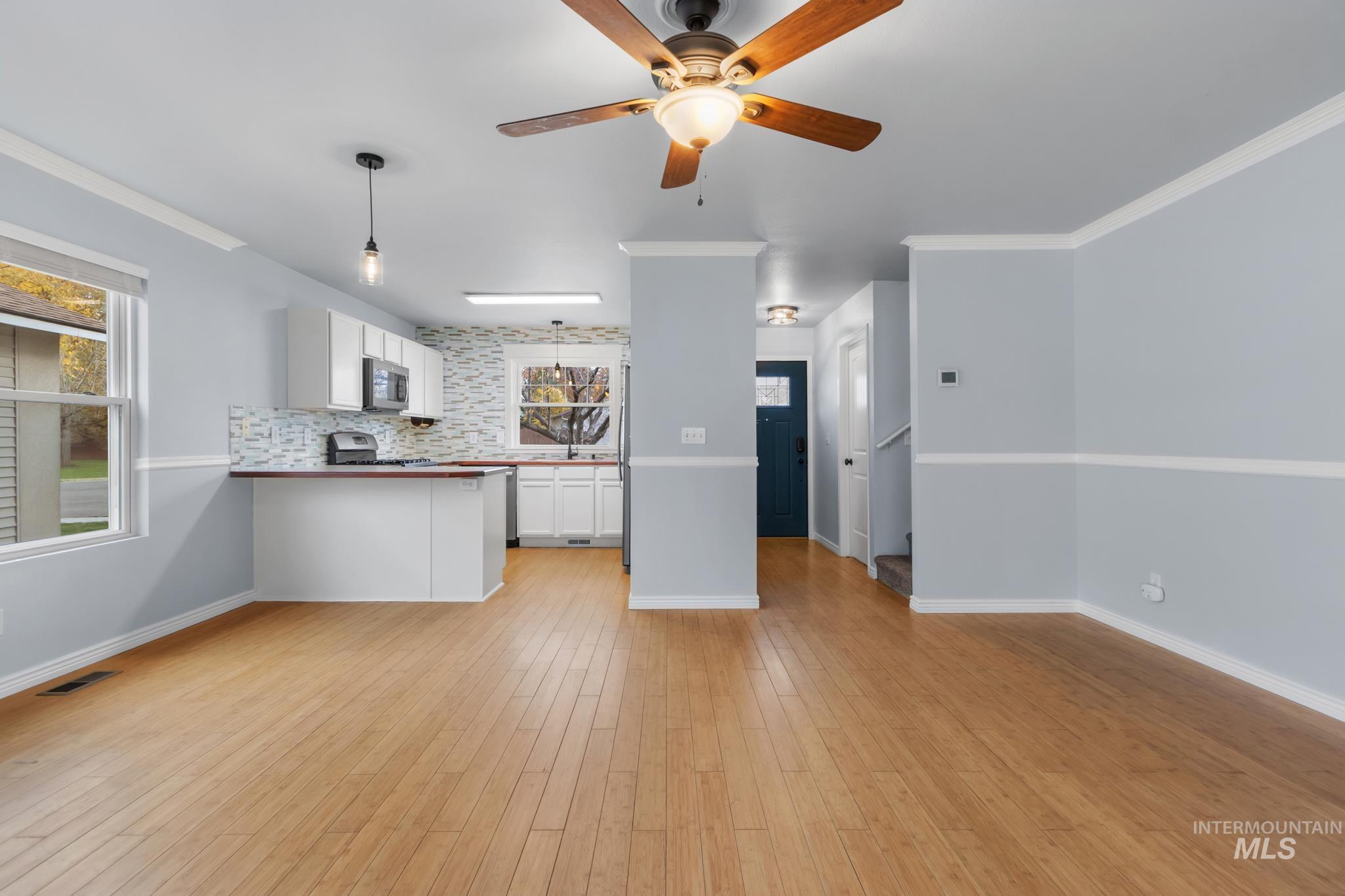 Kitchen with hanging light fixtures, white cabinets, crown molding, light wood-style flooring, and a peninsula