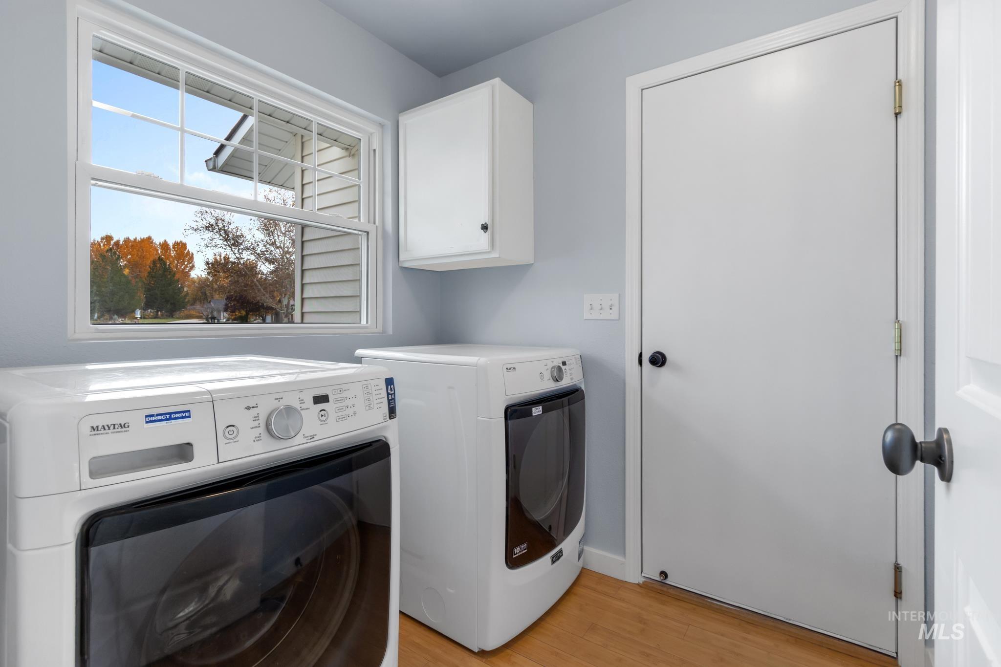 Laundry room with washing machine and clothes dryer, light wood-type flooring, and cabinet space