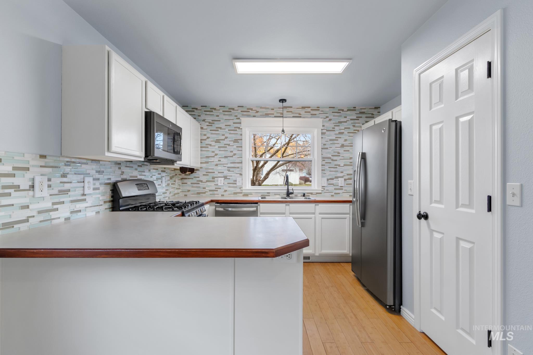 Kitchen with white cabinets, appliances with stainless steel finishes, light countertops, and light wood finished floors