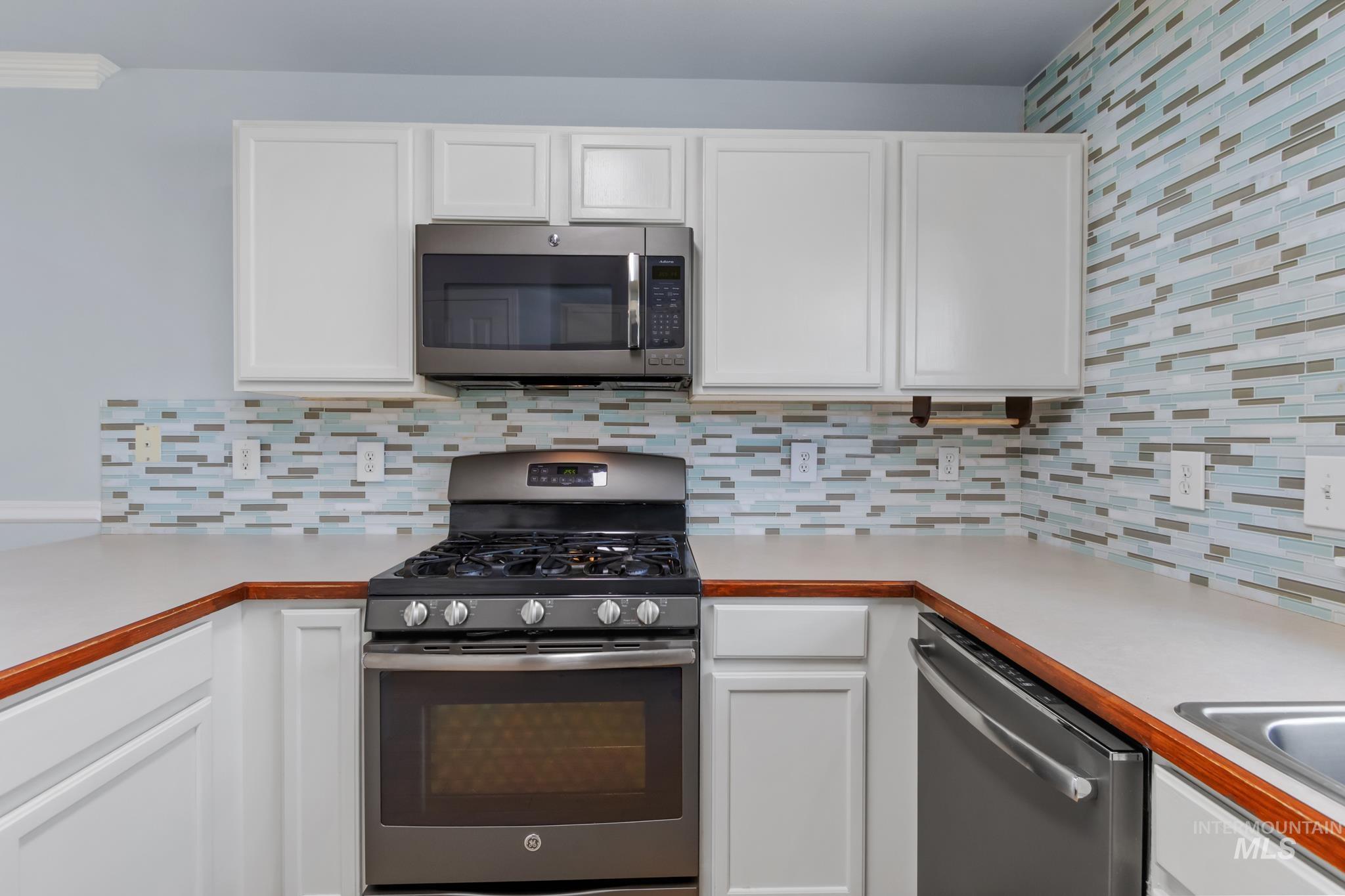 Kitchen featuring appliances with stainless steel finishes, white cabinets, light countertops, and tasteful backsplash