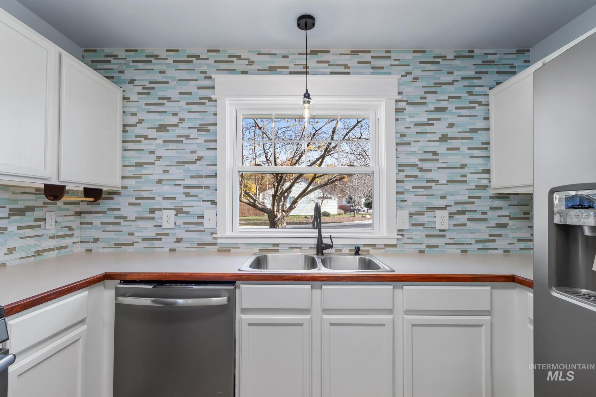 Kitchen with light countertops, appliances with stainless steel finishes, white cabinetry, and decorative backsplash