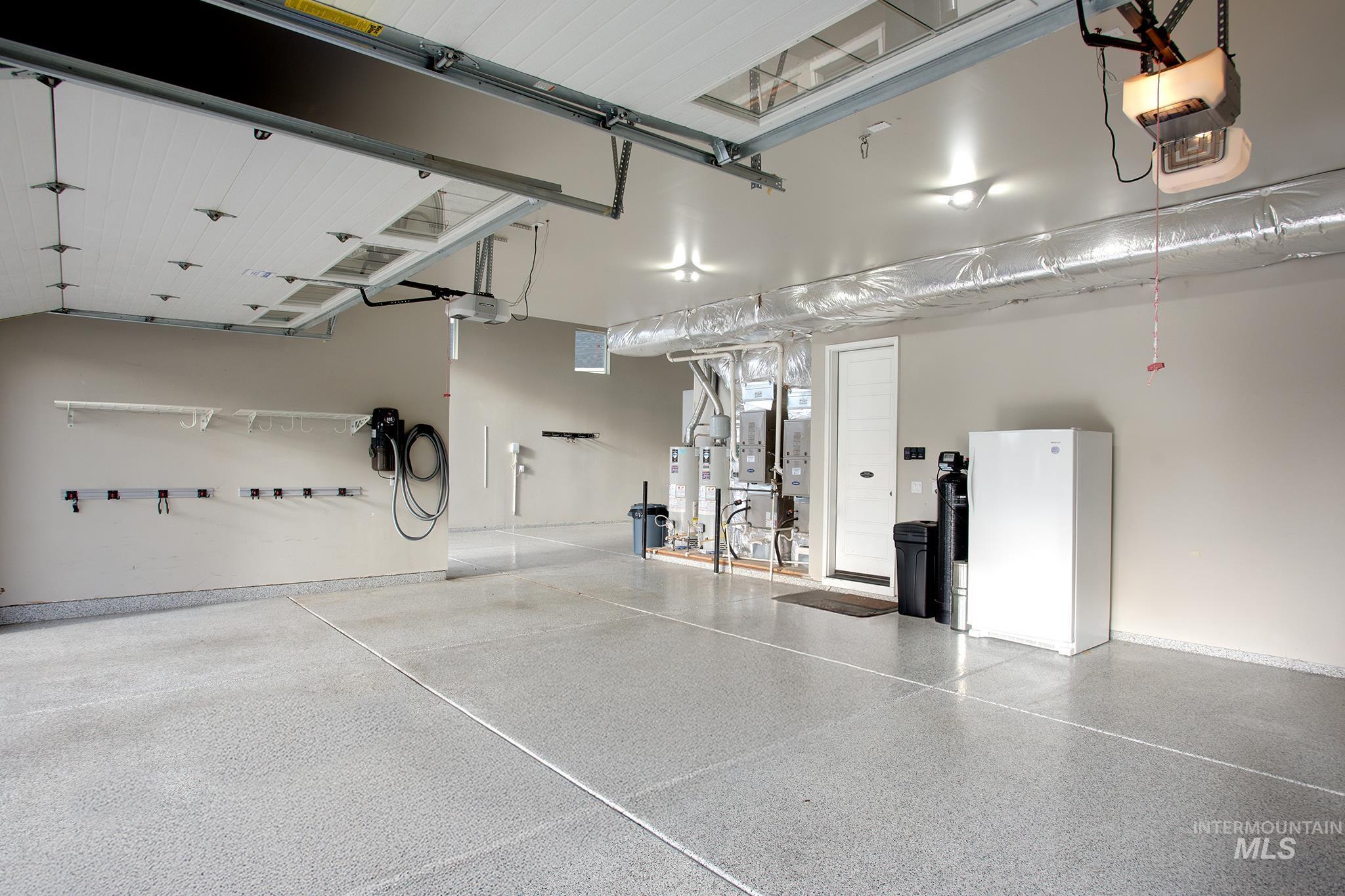 Garage featuring freestanding refrigerator, gas water heater, car charger, and heating unit