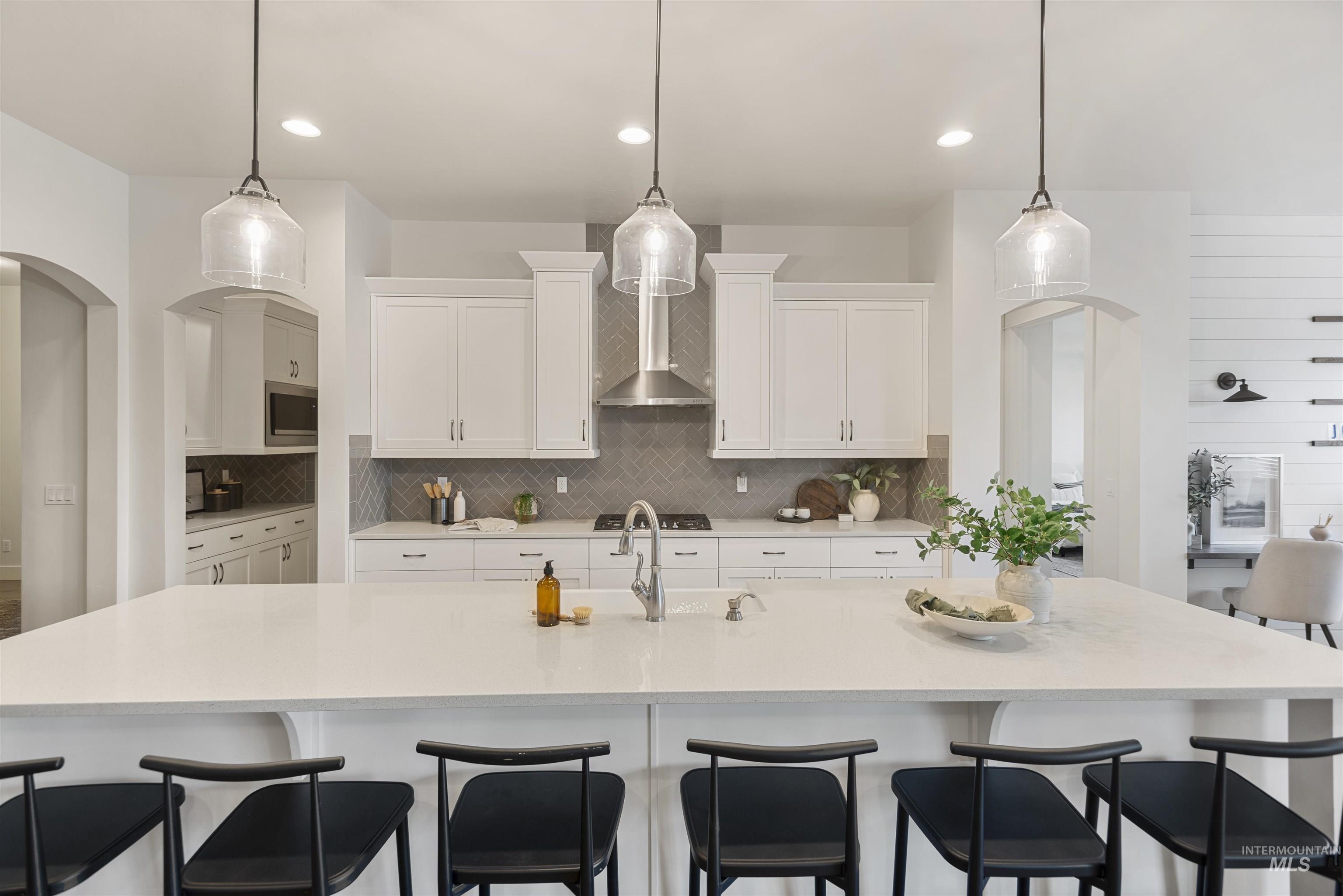 Kitchen with hanging light fixtures, white cabinets, decorative backsplash, and a large island