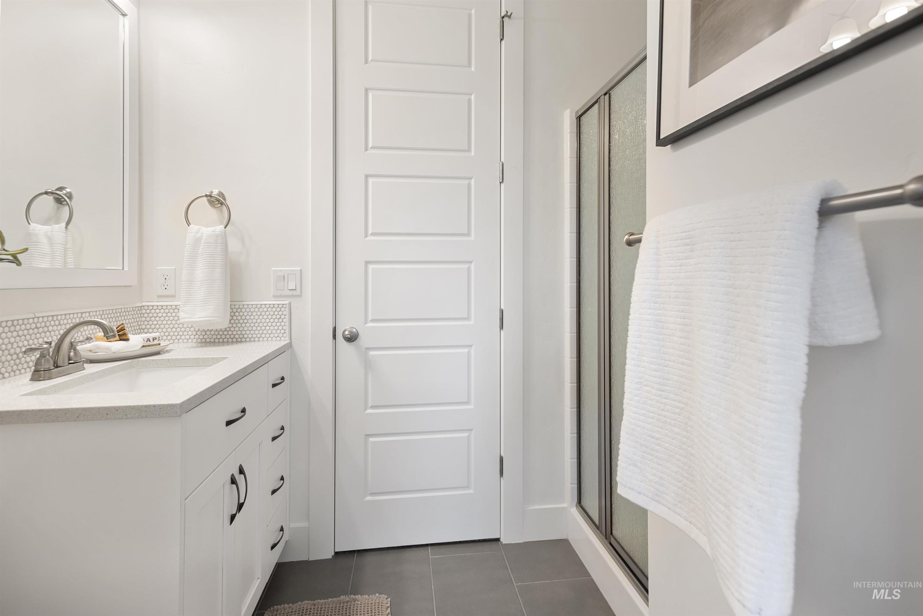 Full bath featuring a stall shower, vanity, dark tile patterned flooring, and tasteful backsplash