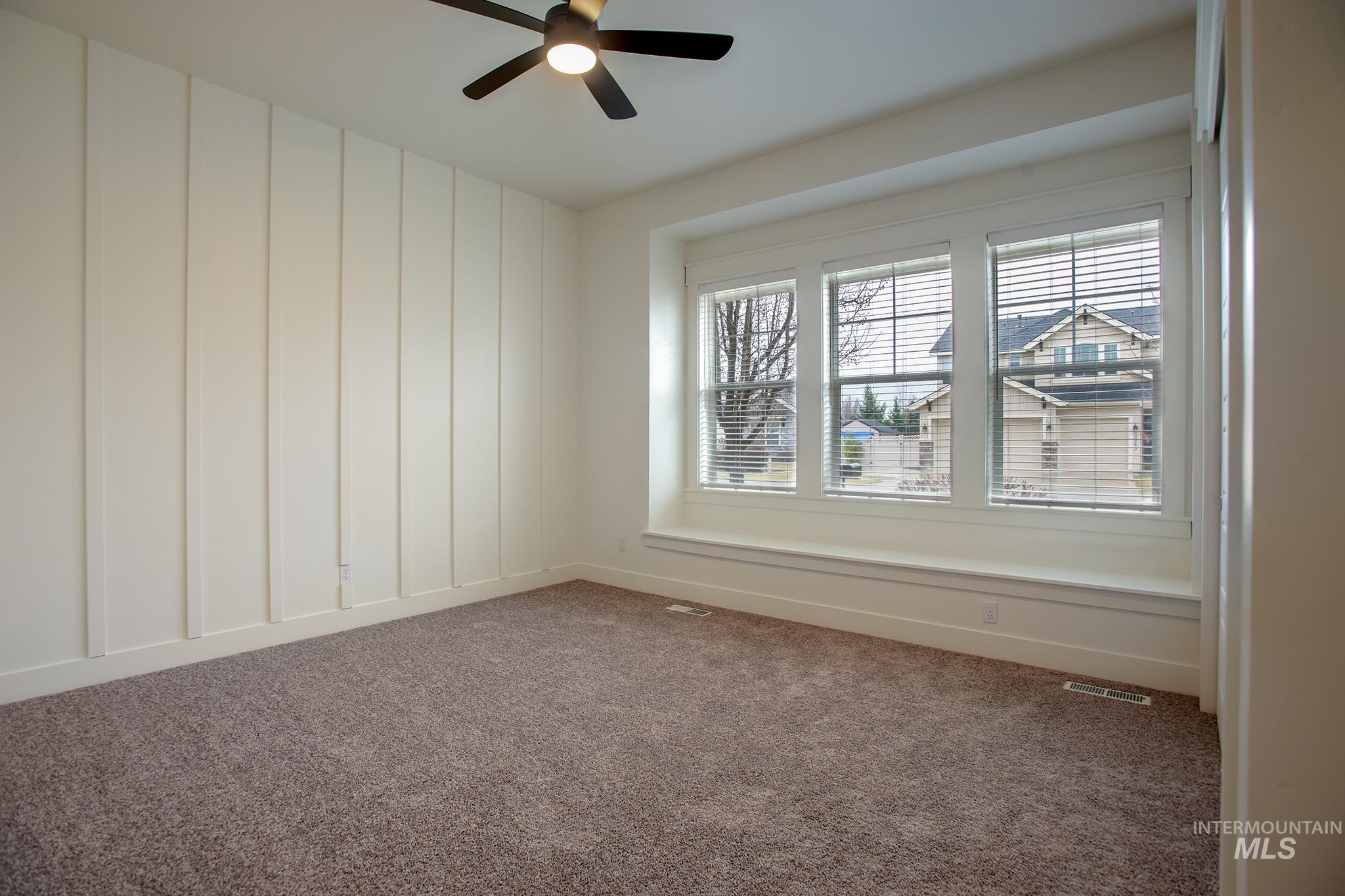 Spare room with dark colored carpet, ceiling fan, and a decorative wall