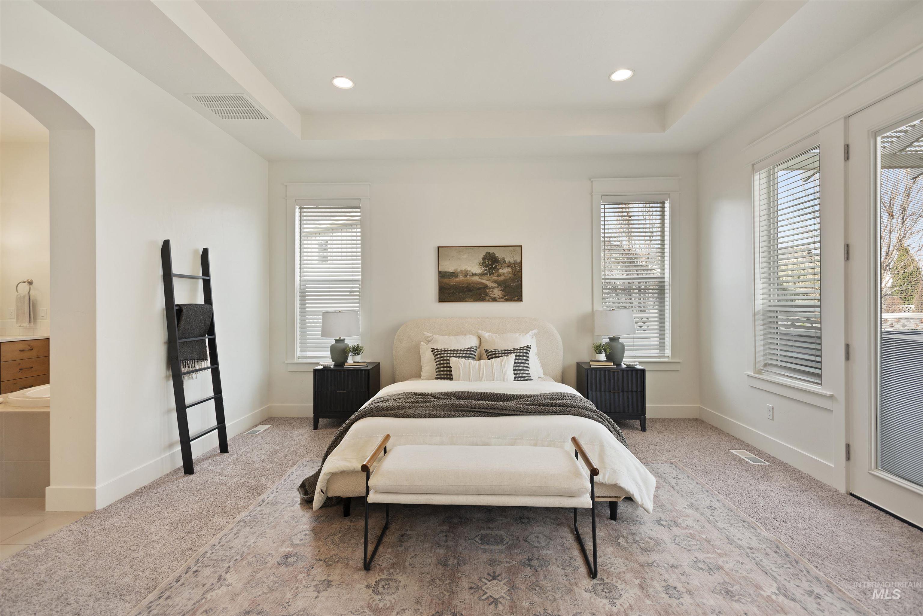 Bedroom with arched walkways, light carpet, recessed lighting, access to exterior, and a raised ceiling