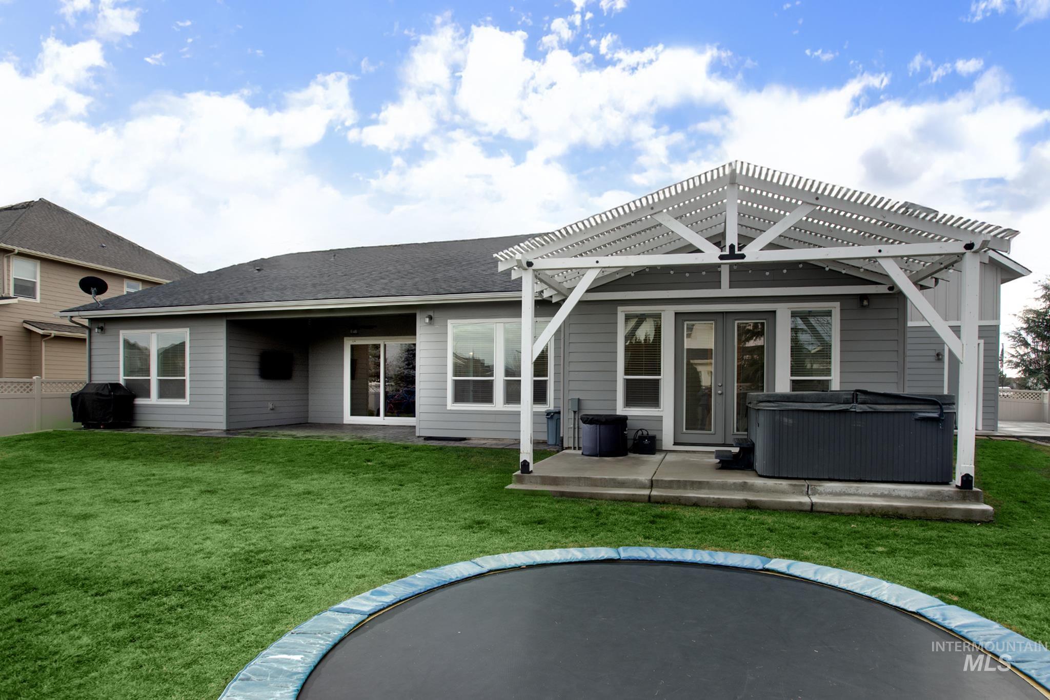 Back of house with a trampoline, a hot tub, a patio, a pergola, and a shingled roof